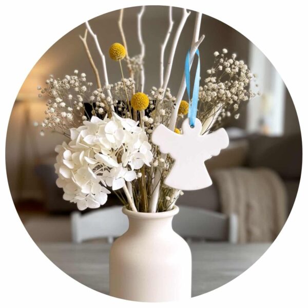 Keramieken engel met blauw lint hangend in een boeket met droogbloemen