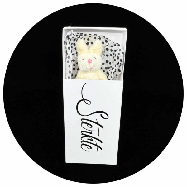 Konijn in een doosje met de tekst 'Sterkte' tegen een zwarte achtergrond.